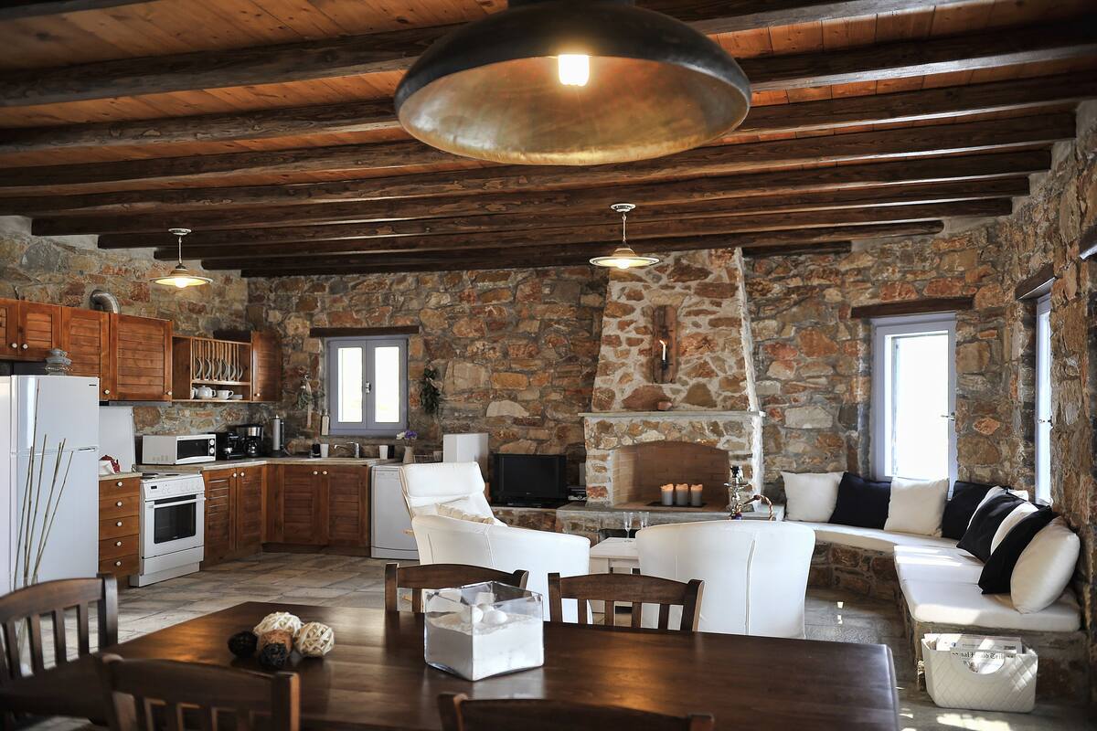 A rustic kitchen with stone walls, wooden beams, and a large hanging light fixture.