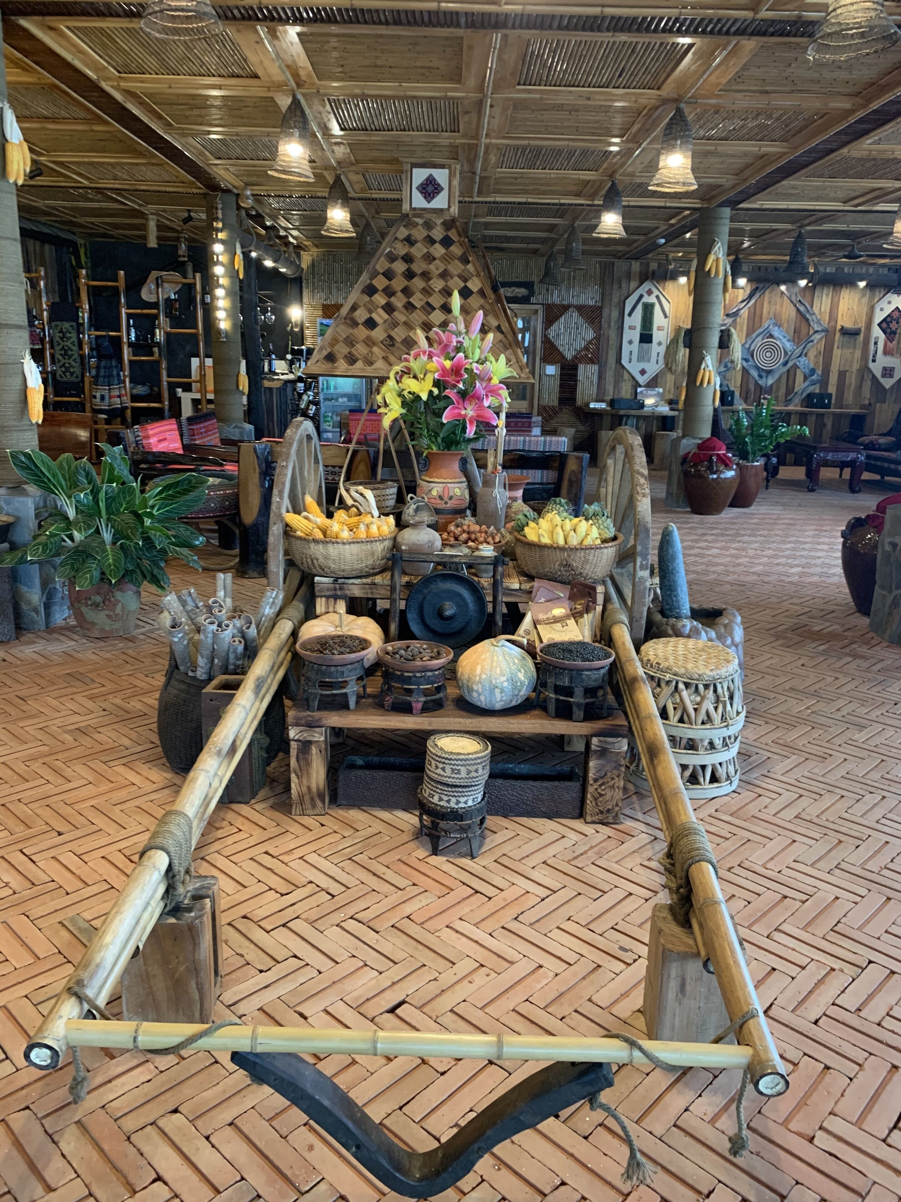 A rustic interior with a central display of traditional items, including a large vase of flowers, baskets of fruits, and various wooden objects.
