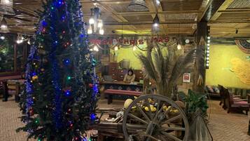 A rustic interior with a decorated Christmas tree, wooden furniture, and a vintage cart.