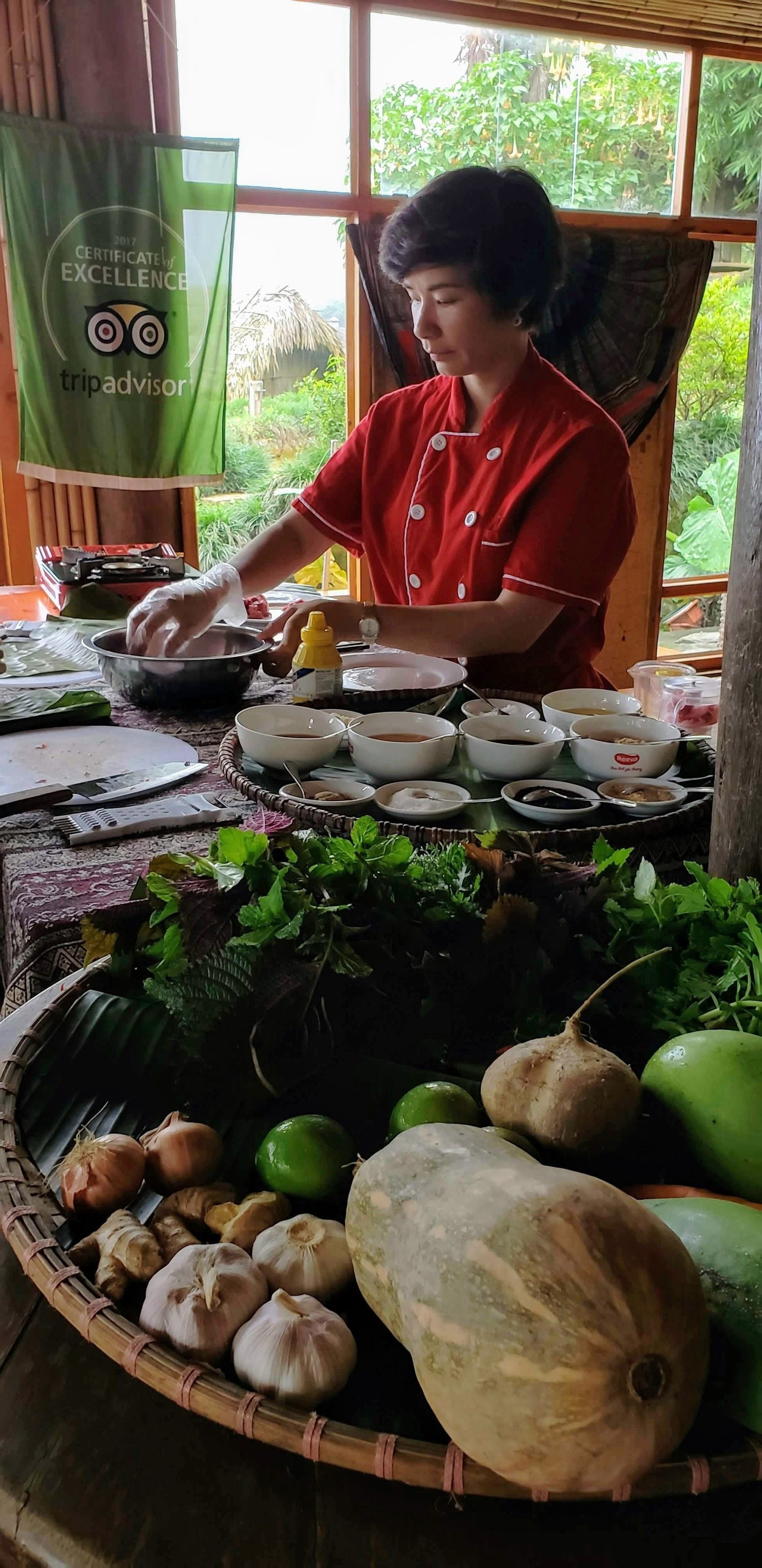 A person preparing food at a table with various bowls and ingredients, including vegetables and a basket of fresh produce.