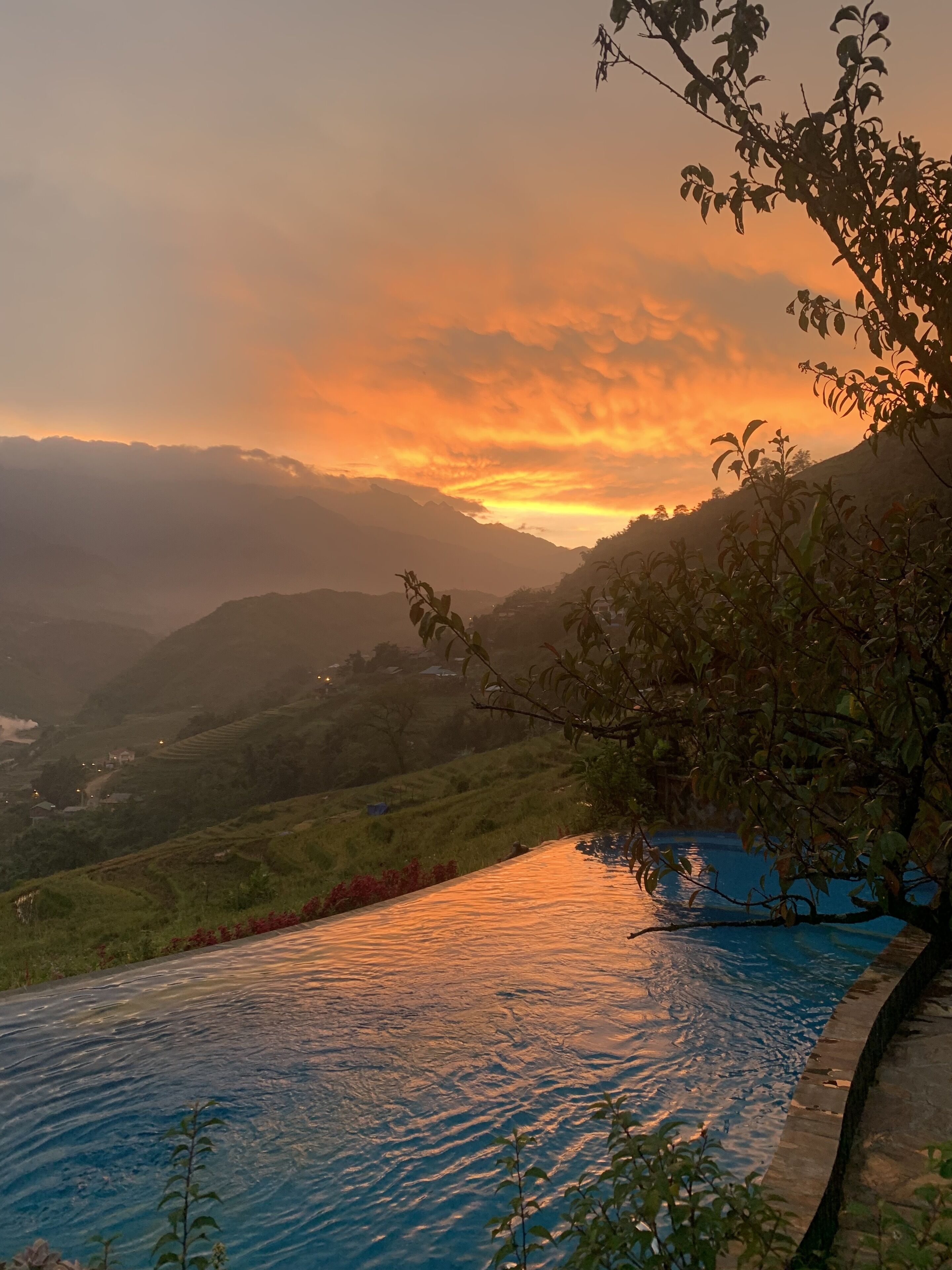 Un paisaje sereno con un cuerpo de agua que refleja el atardecer, rodeado de abundante vegetación y colinas lejanas.