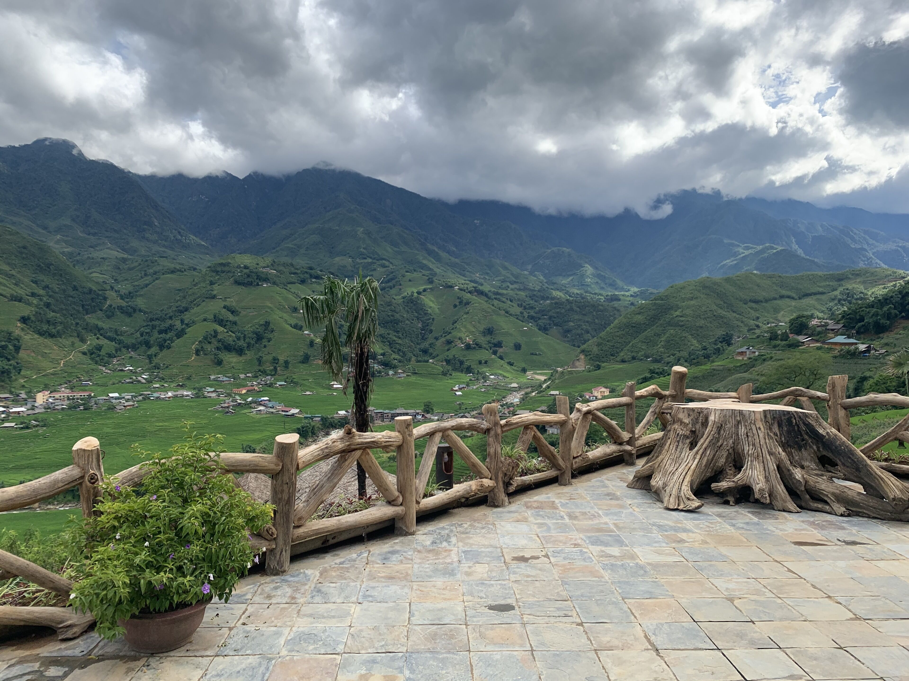 A stone-paved terrace with a wooden fence overlooking a mountainous landscape.