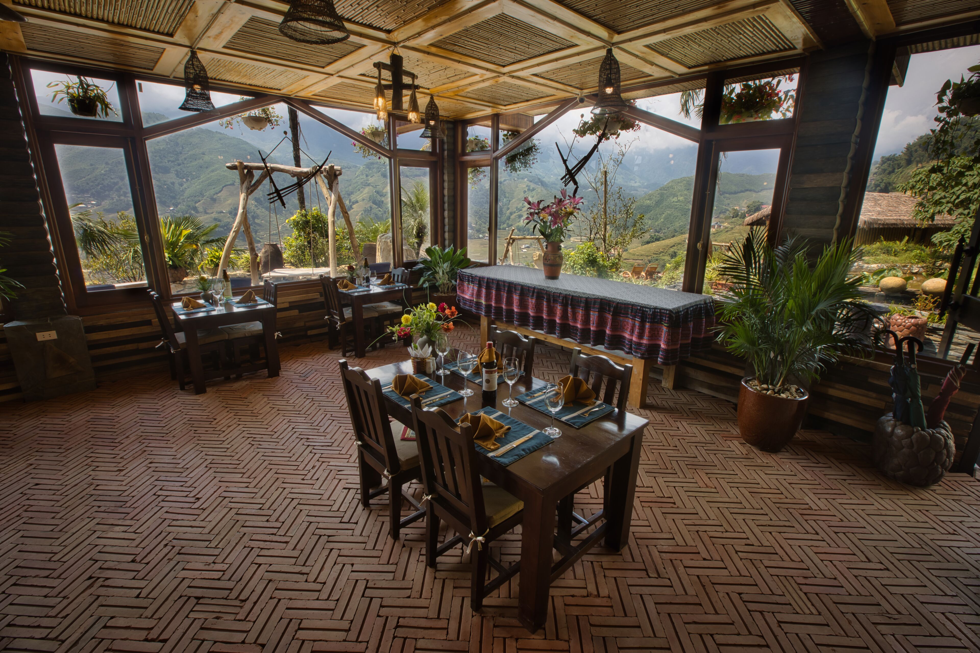 A dining area with a wooden table set for four, surrounded by large windows offering a view of a mountainous landscape.