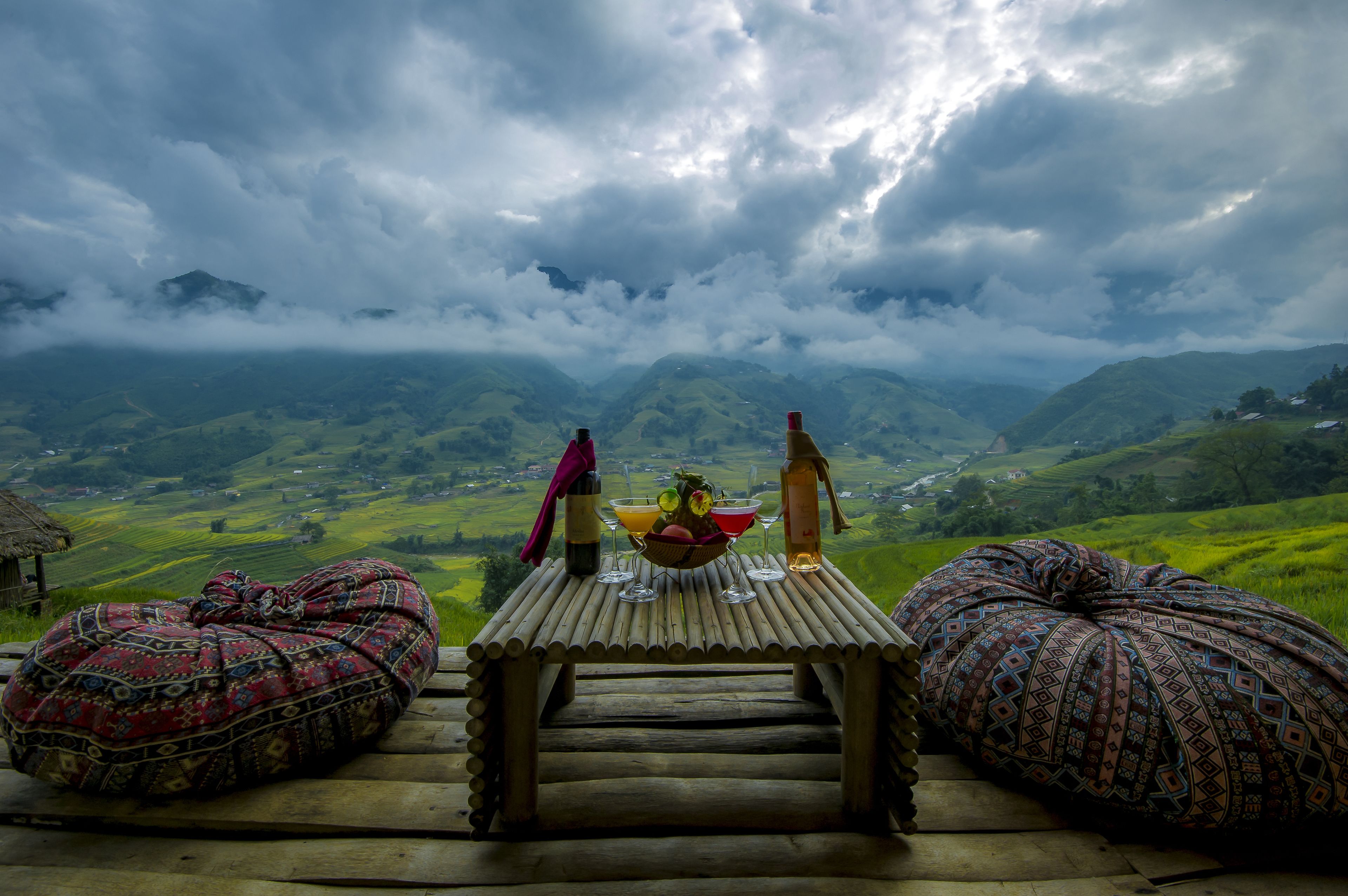 A wooden table with a bottle and glasses, set against a mountainous backdrop.