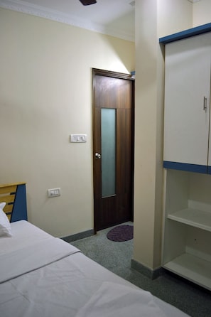 A bedroom with a bed, a wardrobe, a door, and a wall socket. - Metro Park (Chennai)