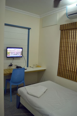 A single bed, a desk with a computer, and a window with blinds. - Metro Park (Chennai)