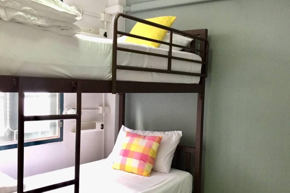 Habitación con literas, ventana y aire acondicionado de pared, con un cojín a cuadros.