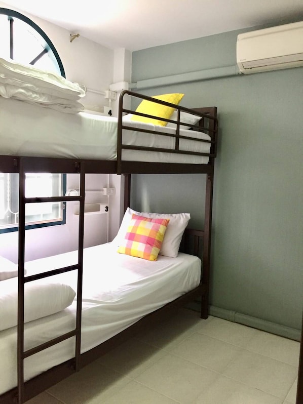Habitación con literas, ventana y aire acondicionado de pared, con un cojín a cuadros.