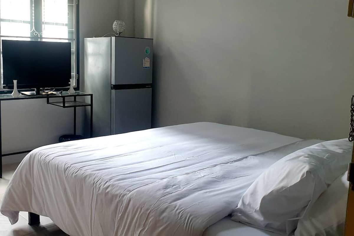Un dormitorio con una cama, un televisor sobre un mueble bajo y un refrigerador.