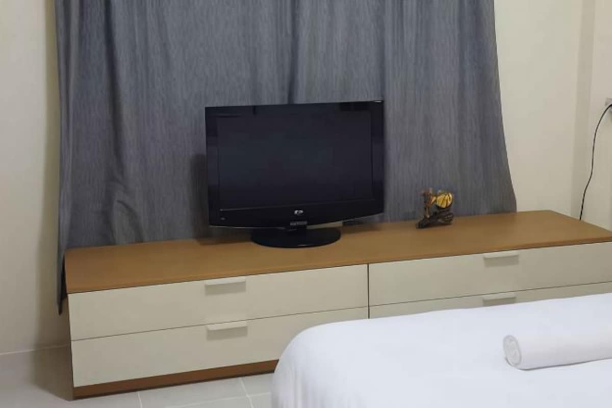 Un dormitorio con una cama, un televisor sobre un aparador de madera y una cortina.