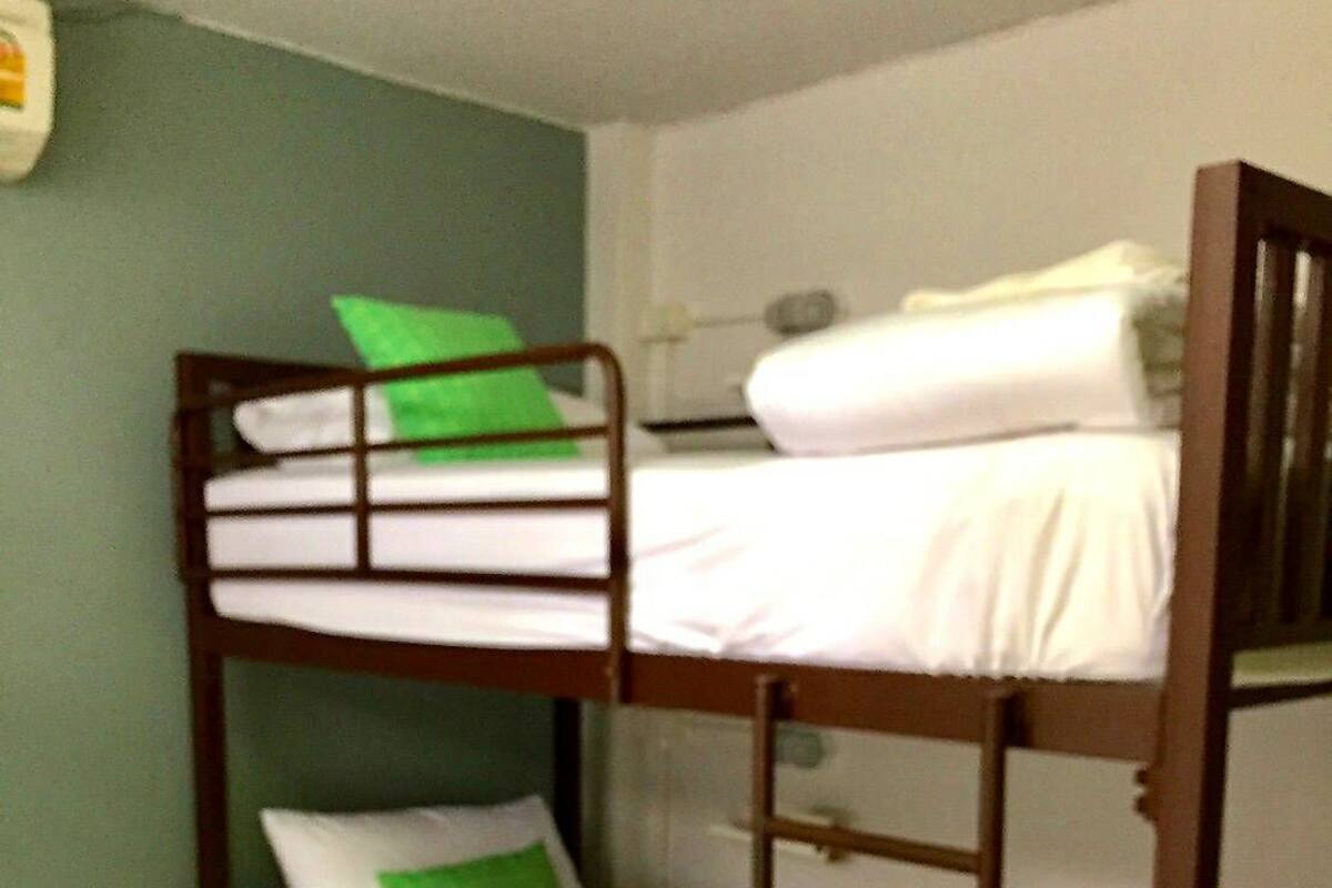 Dormitorio con literas, almohada verde y ropa de cama blanca.