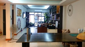 A spacious living area with a large dark wooden table, a fan, and a bookshelf. - Asoke Montri Hostel (Bangkok)
