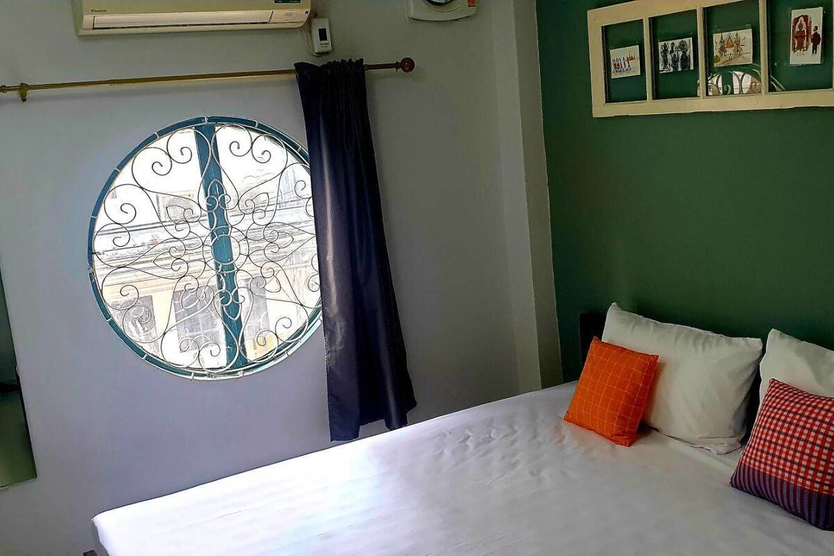 Un dormitorio con cama, ventana con cortinas, aire acondicionado de pared y un estante con fotografías.