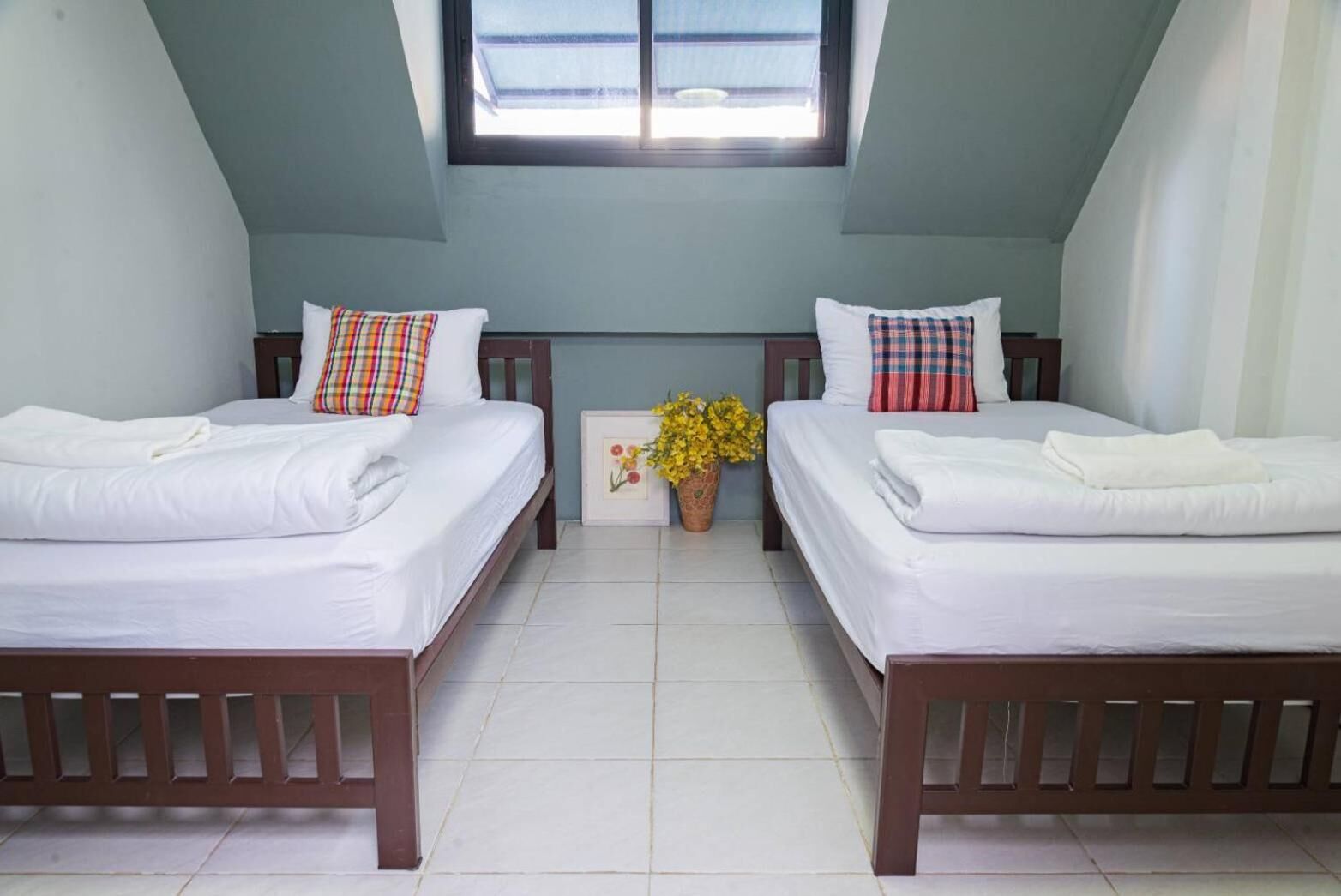 A room with two beds, a window, and a potted plant.