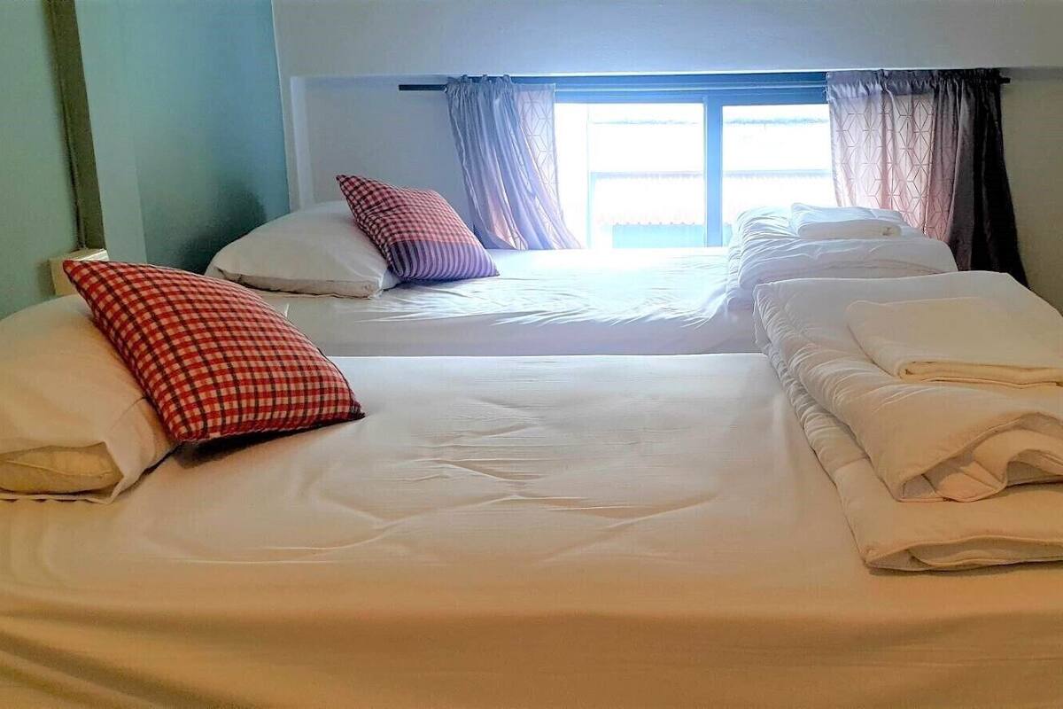 Habitación de hotel con dos camas, cada una con ropa blanca y almohada a cuadros rojos.