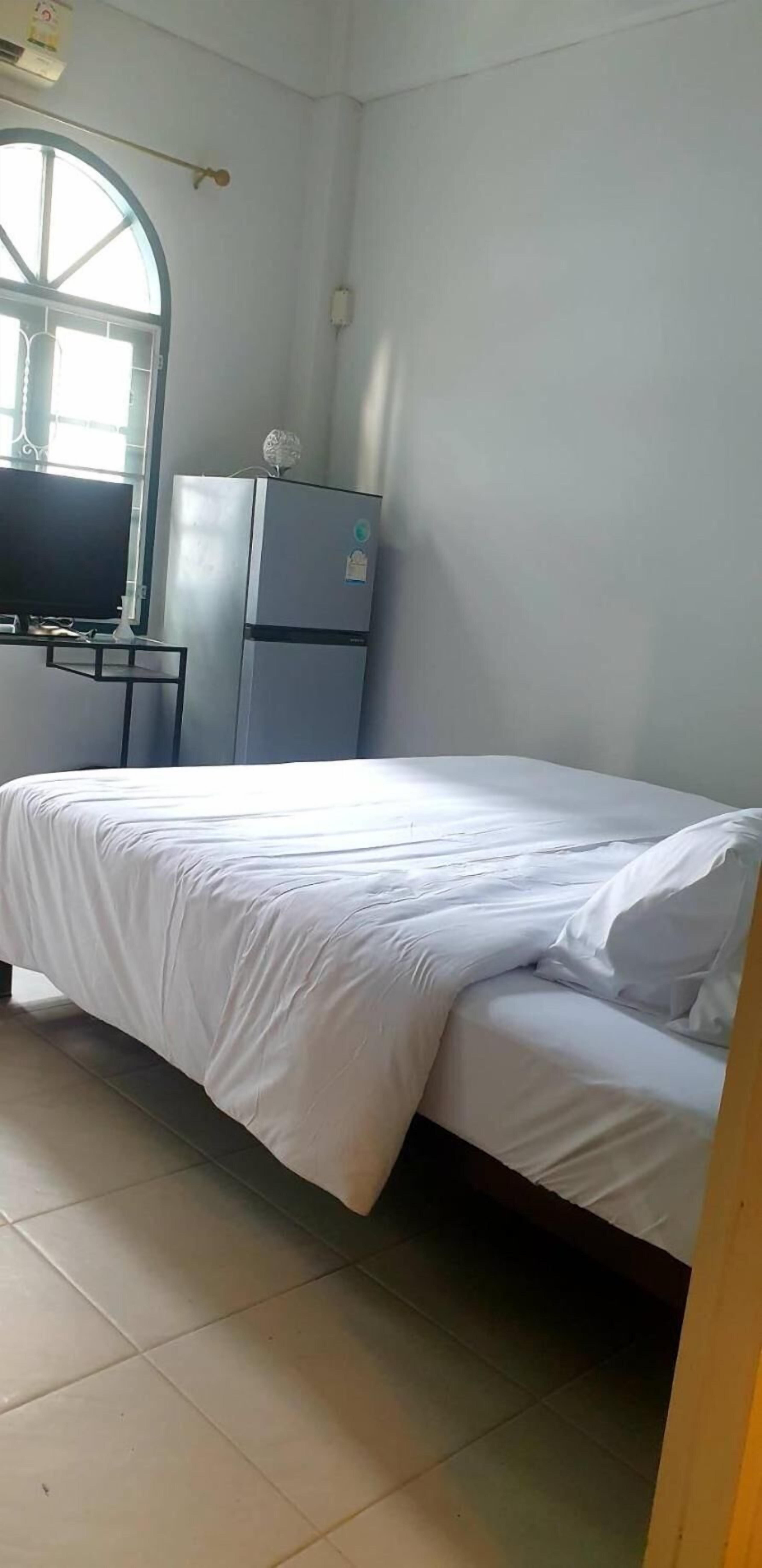 A bedroom with a bed, a television on a stand, a refrigerator, and a window with a view.