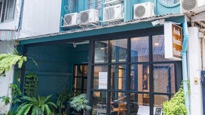 A blue building with multiple air conditioning units, a sign indicating it's a hostel, and potted plants outside. - Asoke Montri Hostel (Bangkok)