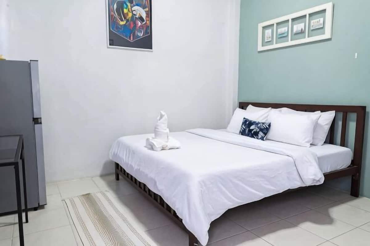 Un dormitorio con cama, una mesita y un refrigerador.