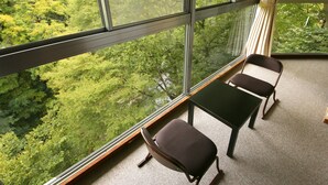 A room with large windows offering a view of a forested area. There is a small table and two chairs. - Hotel Miyama (Chichibu)