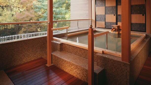 A traditional Japanese onsen with wooden railings, a tiled floor, and a view of the surrounding forest. - Hotel Miyama (Chichibu)