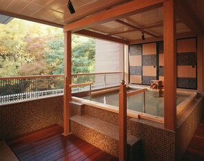 Un onsen japonés tradicional con barandillas de madera, suelo de baldosas y vistas al bosque circundante.