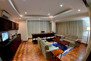 A living room with a sofa, a coffee table, a TV, and a dining table. - Golden Butterfly Hotel (Yangon)