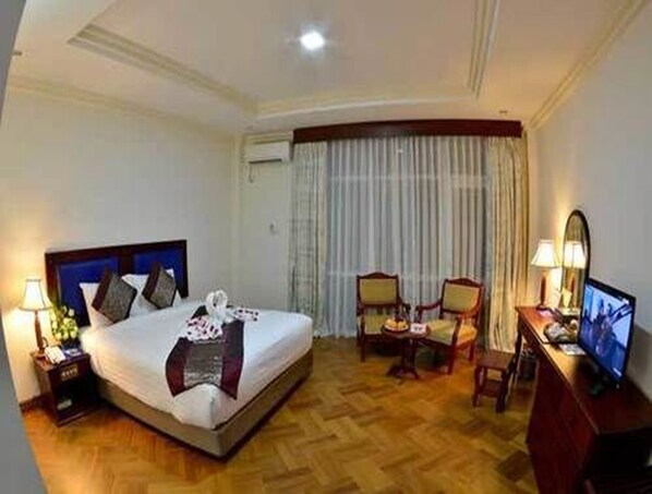 A hotel room with a bed, two chairs, a desk with a computer, and a TV. - Golden Butterfly Hotel (Yangon)
