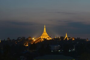 A large, illuminated pagoda with a pointed spire, surrounded by trees and buildings. - Golden Butterfly Hotel (Yangon)