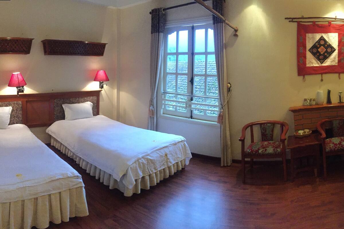 Une chambre d’hôtel avec deux lits simples, un bureau avec une chaise, une télévision et une fenêtre avec des rideaux.