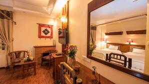 A hotel room with a wooden floor, a large mirror, a TV, a desk with a vase of flowers, two chairs, and a bed with a headboard. - Thai Binh Sapa Hotel (Sa Pa)