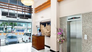 A hotel lobby with a modern chandelier, a reception desk, an elevator, and a decorative wall piece. - The Hub Hotel (Yangon)