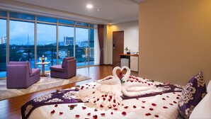 A hotel room with a large bed, two armchairs, a small table, and a view of the cityscape through large windows. - The Hub Hotel (Yangon)