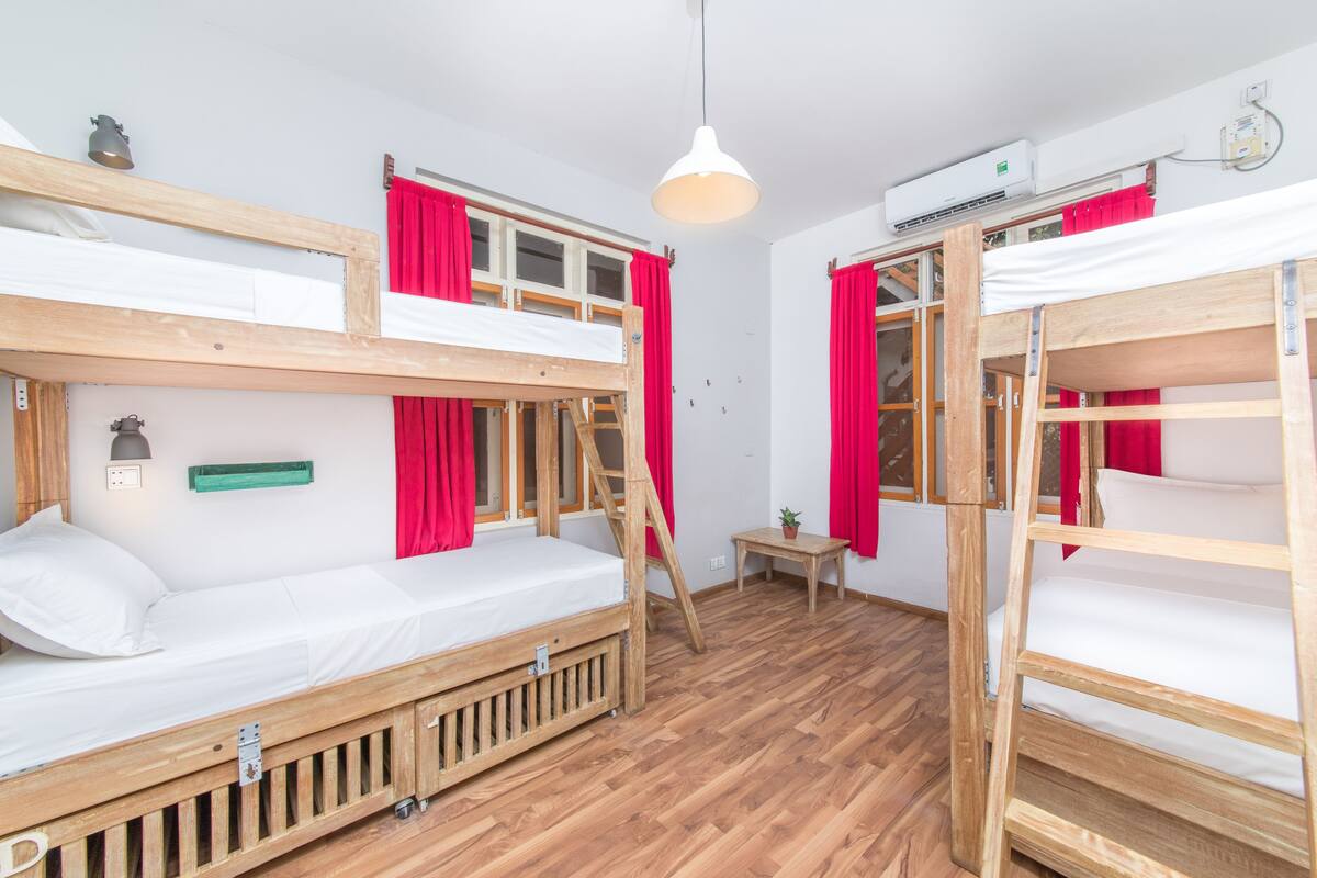 Ein Zimmer mit zwei Etagenbetten, Holzboden, einem kleinen Tisch mit Pflanze und einer Pendelleuchte.
