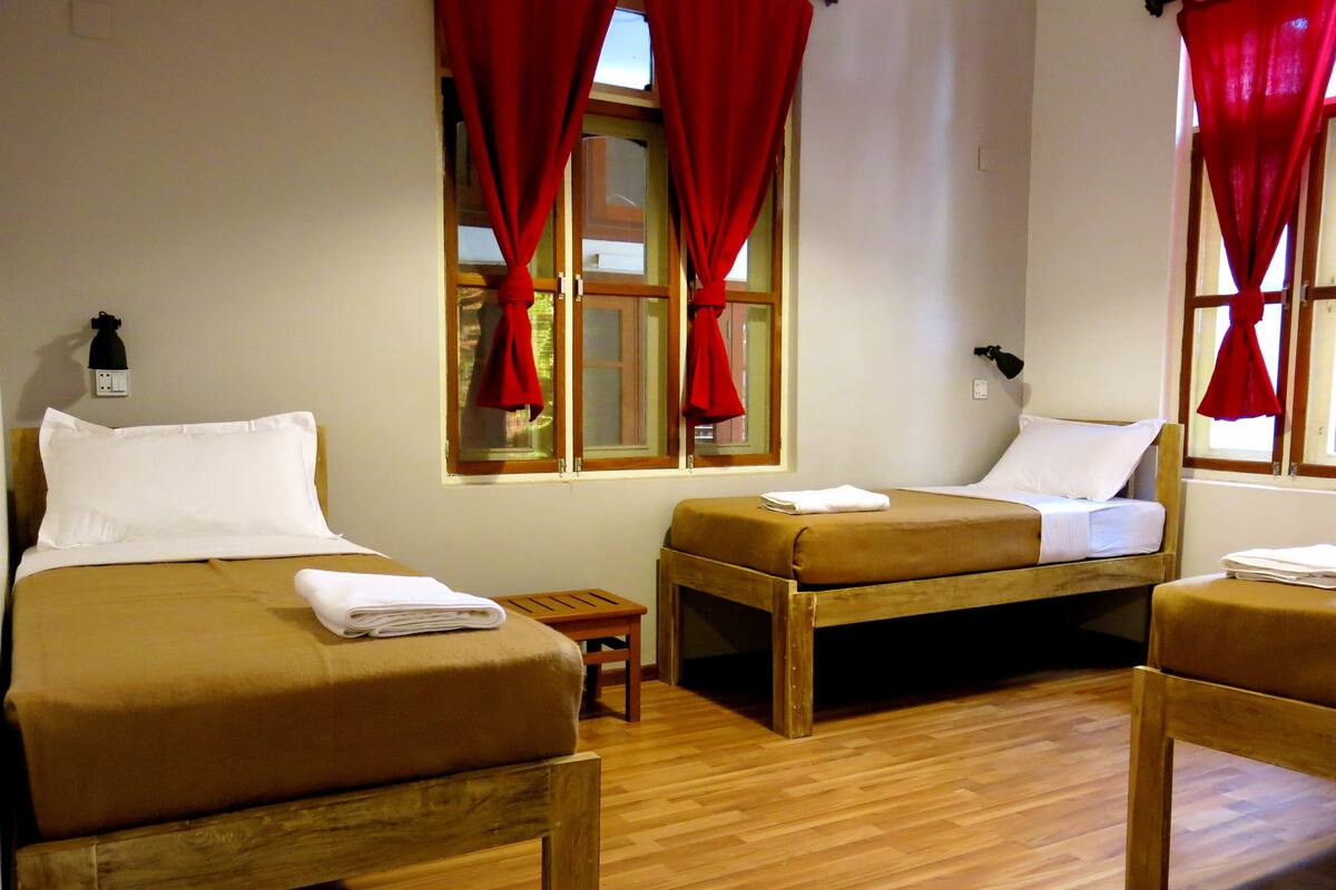 Ein Zimmer mit zwei Holzbetten, einem kleinen Holztisch und roten Vorhängen an den Fenstern.