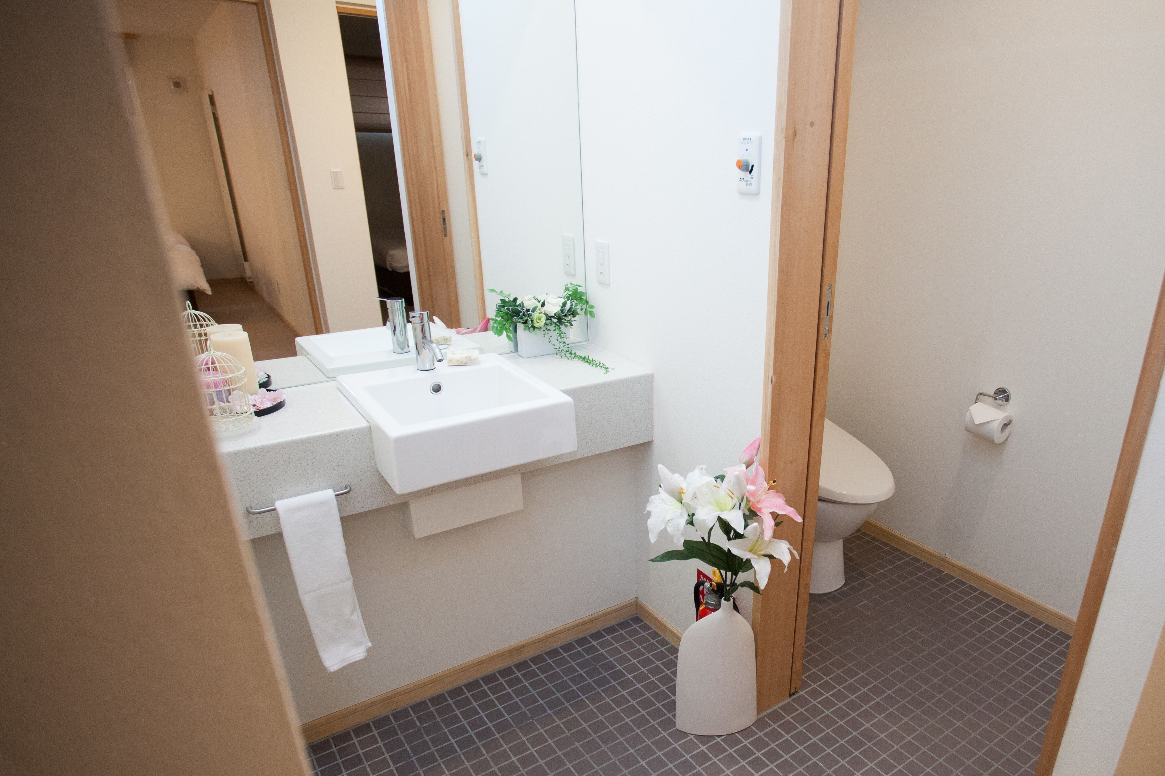 Un baño con un lavamanos blanco, un inodoro y un espejo. Hay una toalla colgada en la pared y un florero con flores en la encimera.