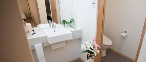 Un baño con un lavamanos blanco, un inodoro y un espejo. Hay una toalla colgada en la pared y un florero con flores en la encimera.