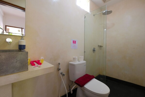 Casa de banho com sanita, cabine de duche em vidro, lavatório com produtos de higiene e espelho.