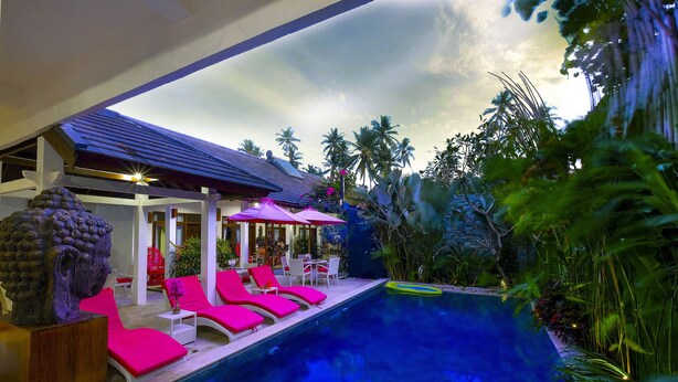 A pool area with pink lounge chairs, a Buddha statue, and a covered seating area with umbrellas. - Lombok Senggigi Hotel (Senggigi)