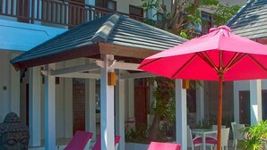 A covered outdoor seating area with a red umbrella, white lounge chairs, and a wooden pergola. - Lombok Senggigi Hotel (Senggigi)