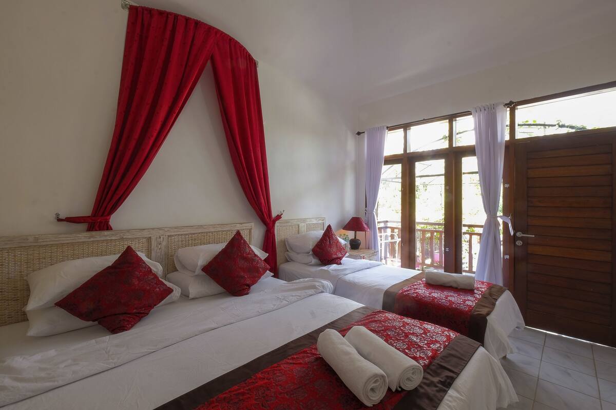 Een hotelkamer met twee bedden, rode gordijnen, wit beddengoed en een houten deur.