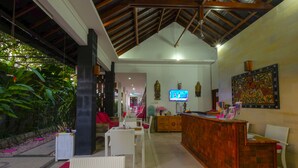 A reception area with a wooden desk, white wicker chairs, a TV, and a large framed artwork on the wall. - Lombok Senggigi Hotel (Senggigi)