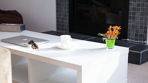 Un tavolo bianco con un portatile, una tazza bianca e un vaso verde con fiori.