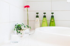 A bathroom with a white bathtub, a potted plant, a glass candle, and green bottles of shampoo and conditioner. - Shirokuma 1 (Kutchan)