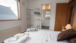Una camera d'albergo con un letto, una finestra, un mobiletto a scaffali in metallo, una porta in legno e un comodino con una lampada.