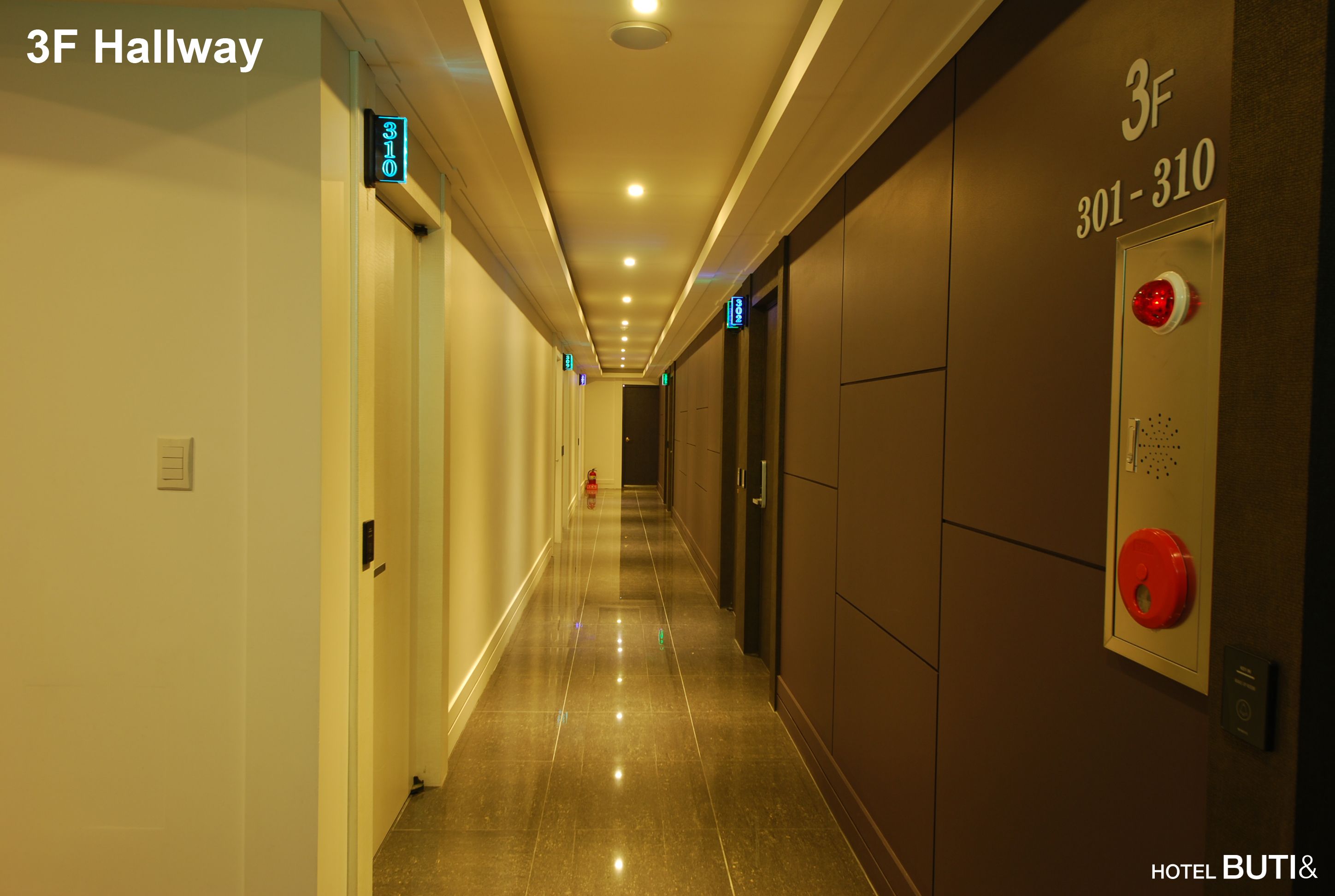 A hotel hallway with a sign indicating room 3F, a fire alarm, and a door with a number plate.