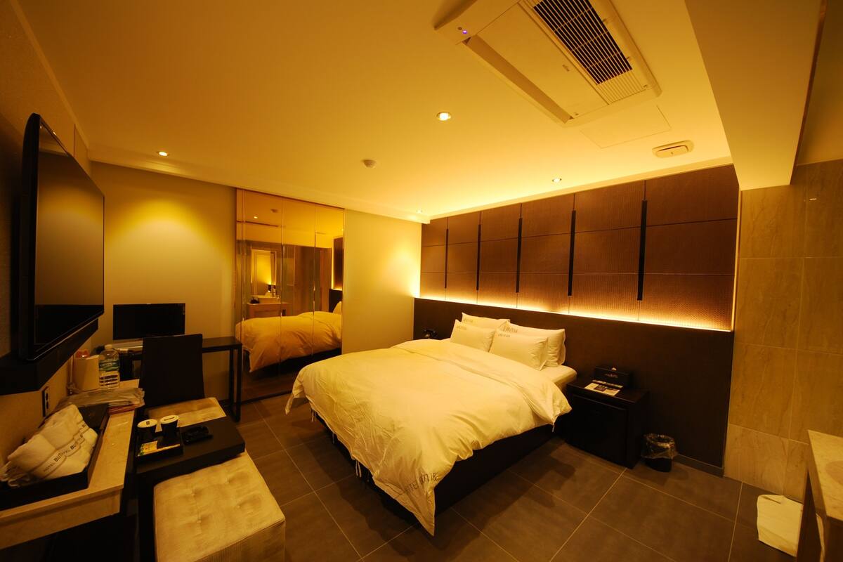 Une chambre d’hôtel moderne dotée d’un grand lit, de tables de chevet, d’une télévision et d’une salle de bain avec un miroir et un lavabo.