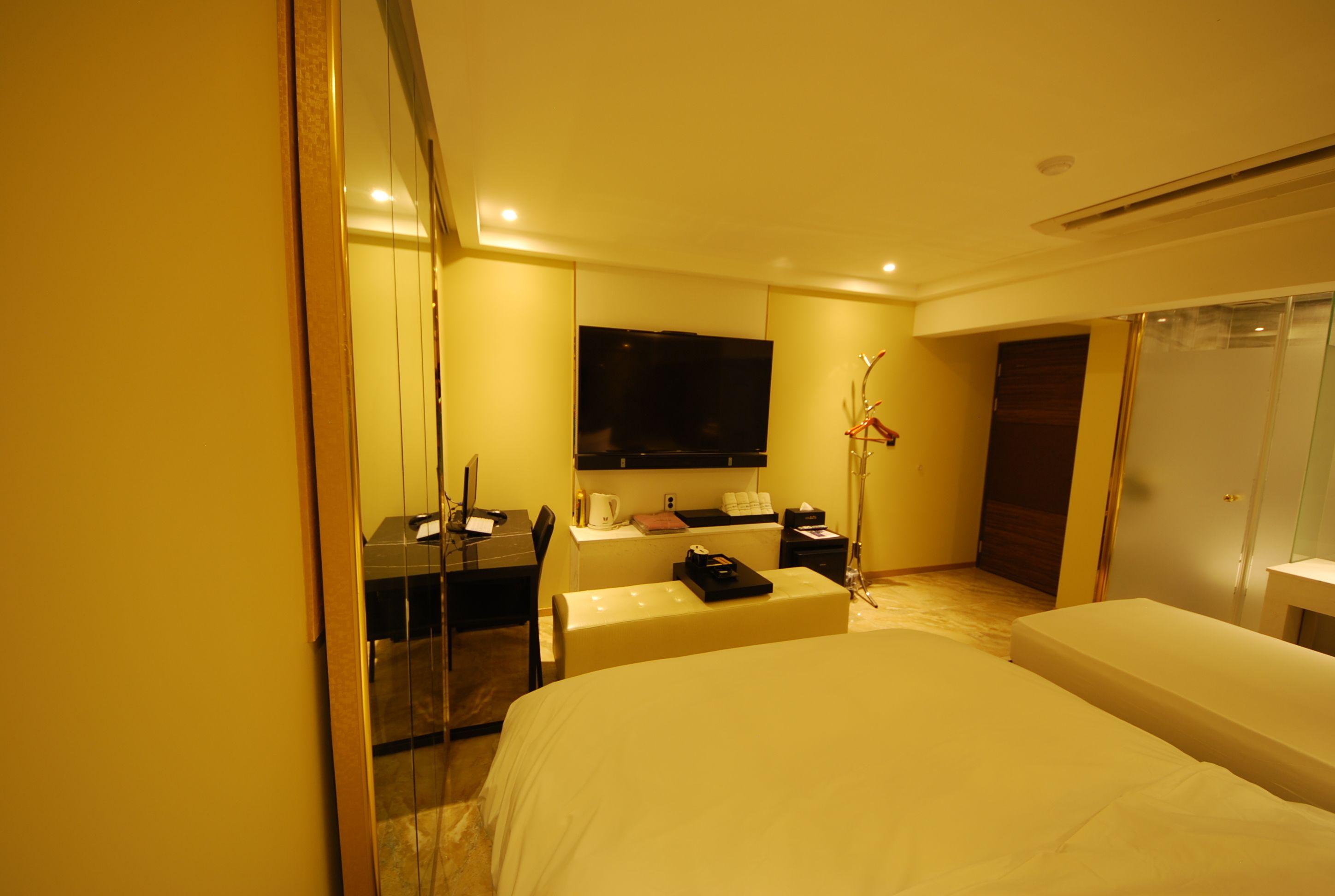 A hotel room with a large bed, a desk with a computer, a flat-screen TV, and a bedside table.