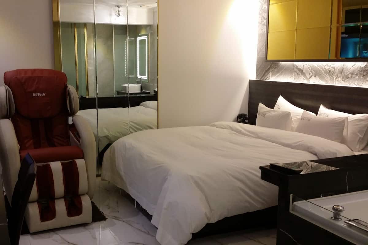 Une chambre d’hôtel équipée d’un lit, d’un fauteuil massant, d’un bureau avec un ordinateur et d’une salle de bain avec baignoire.