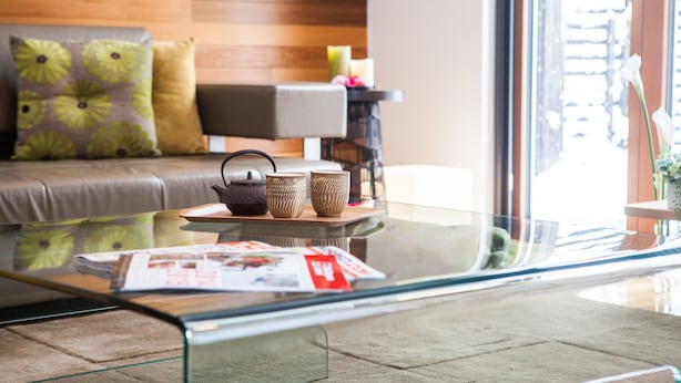 Un salon moderne avec une table basse en verre, un canapé agrémenté de coussins à motifs et une table d’appoint ornée d’objets décoratifs.