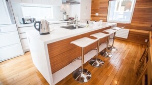 Une cuisine moderne dotée d’un îlot central, de meubles blancs, d’éléments décoratifs en bois et d’une fenêtre qui laisse entrer la lumière naturelle.